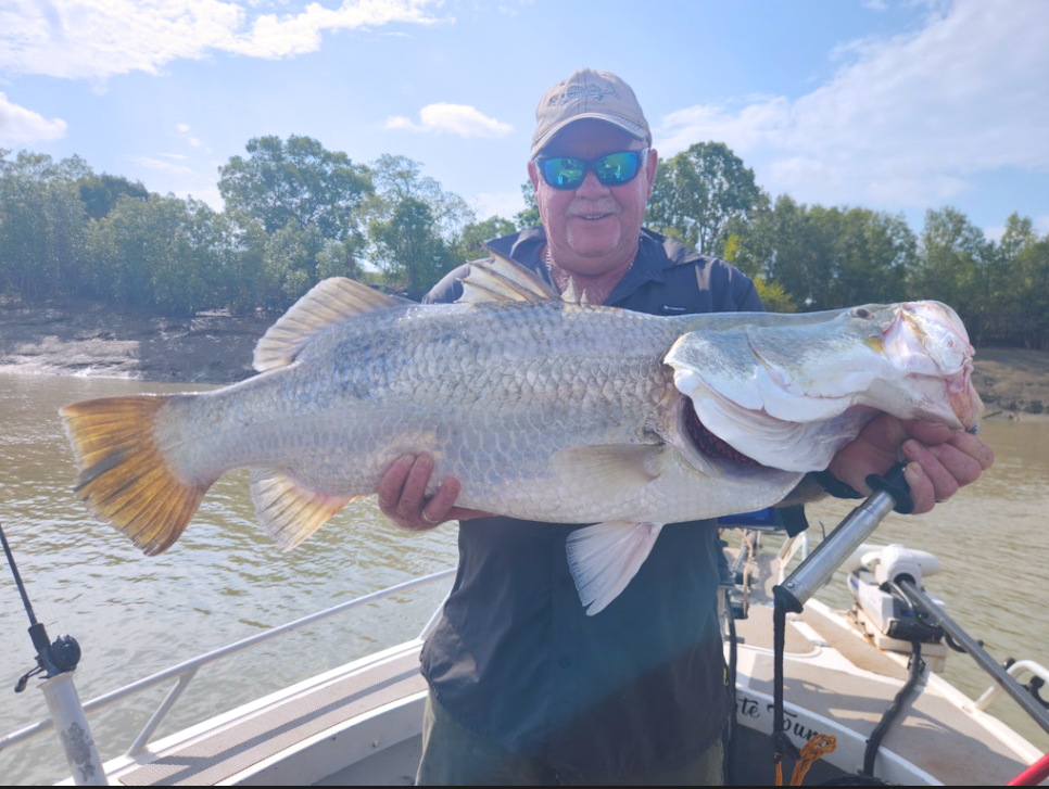 Man holding large fish on a boat in a river setting.