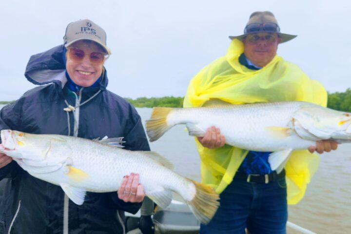 Two people on a boat holding large fish, wearing rain jackets and hats.