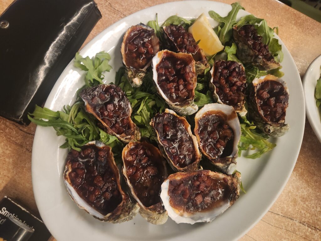 Grilled oysters on a bed of greens with a lemon wedge on a plate.