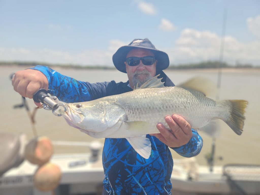 Person holding a large fish on a boat, wearing a blue shirt and hat.