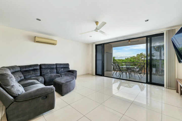 Modern living room with black sofa, TV, balcony view, and sliding glass doors.