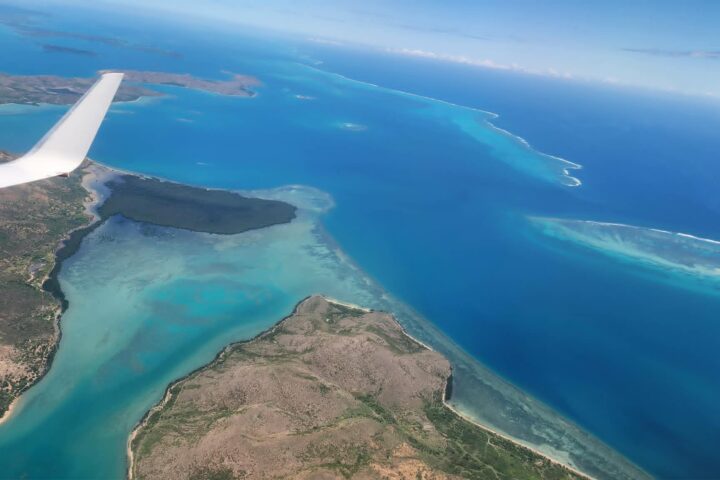 Aerial view of ocean, islands, and airplane wing over clear blue water.