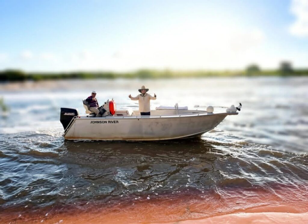 Two people on a small motorboat named 'Johnson Rover' on a sunny day.