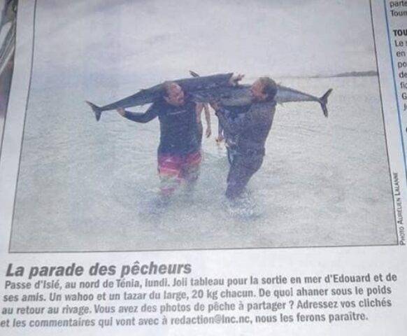 Two men carrying a large fish through shallow water.