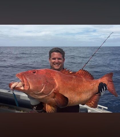 Person holding a large red fish on a boat with ocean background.