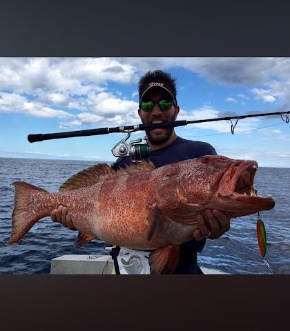 Person holding large fish with fishing rod on a boat.