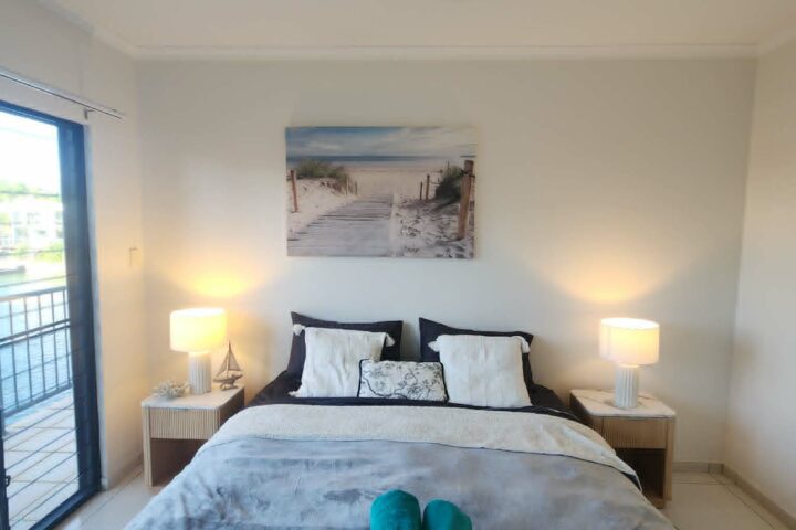 Cozy bedroom with a double bed, pillows, blankets, and two folded towels; bedside lamps illuminate the room.